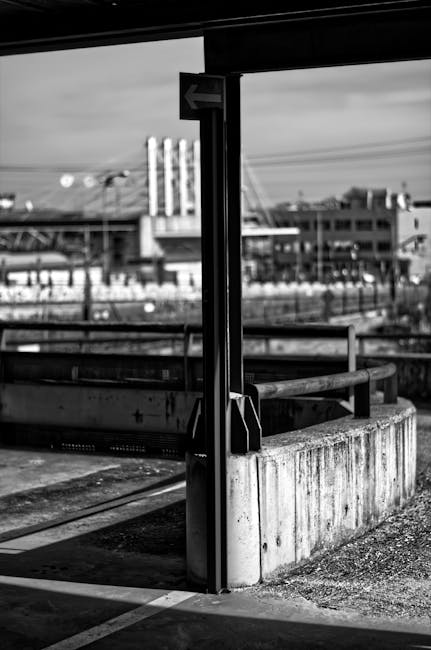 pexels-photo-19286490-19286490 A black and white photo of an abandoned urban railway station with concrete structures and a distant view of a cityscape.